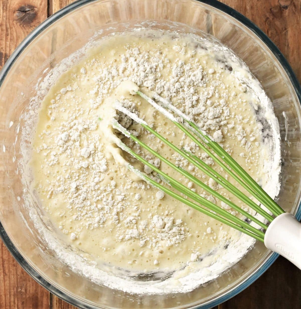 Pancake batter with flour visible and green whisk in large bowl.