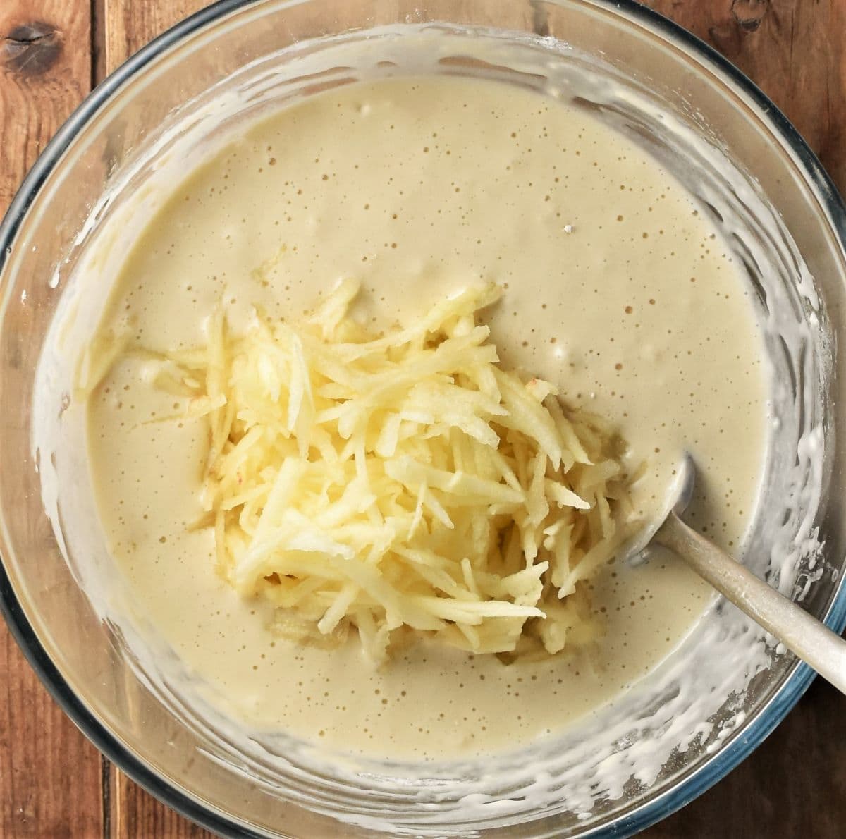 Pancake batter with grated apple and spoon in bowl.