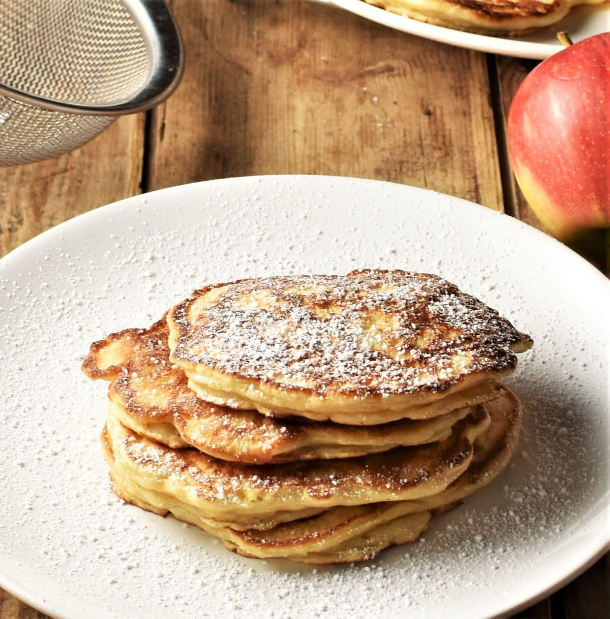 Pancakes dusted with powdered sugar stacked on top of large plate.