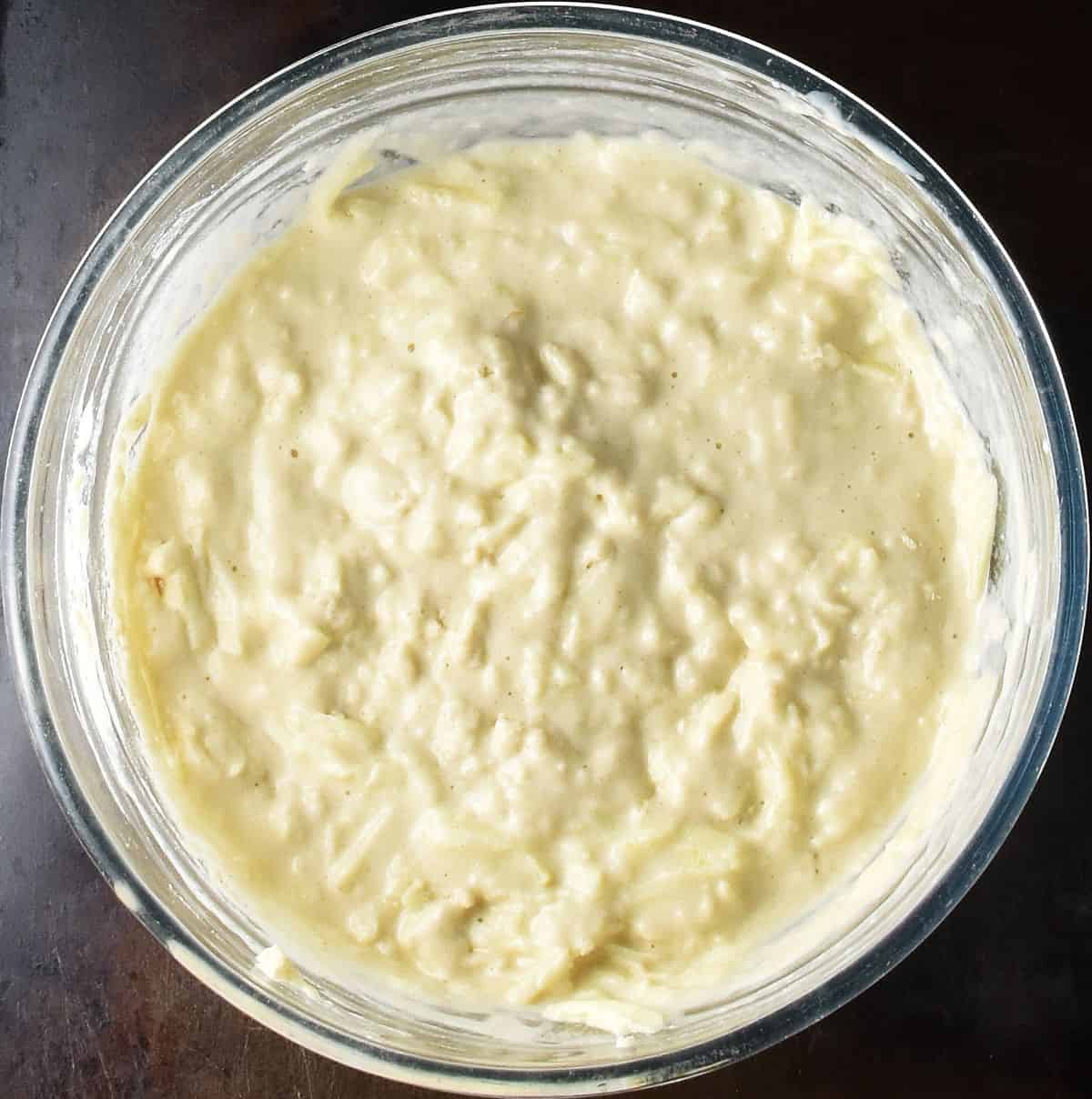 Thick Polish pancake batter with grated apple in large, glass bowl.