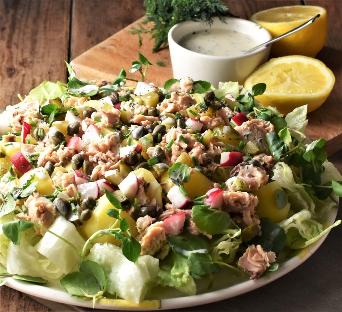 Side view of potato salmon salad with lettuce, lemon and dressing in background.