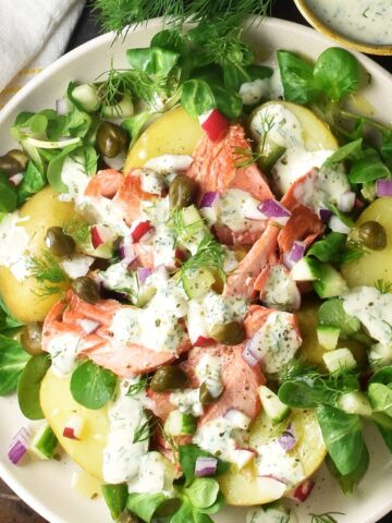 Top down view of salmon and potato salad with creamy dressing on white plate.