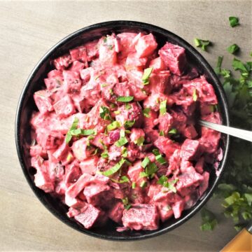 Beet potato salad with parsley in black bowl with spoon.