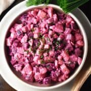 Top down view of creamy beet potato salad in shallow bowl with herbs in background.