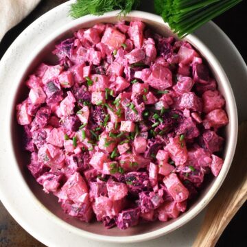 Top down view of creamy beet potato salad in shallow bowl with herbs in background.