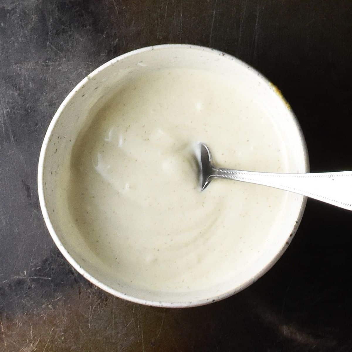 Top down view of creamy dressing mixture in white bowl with spoon.