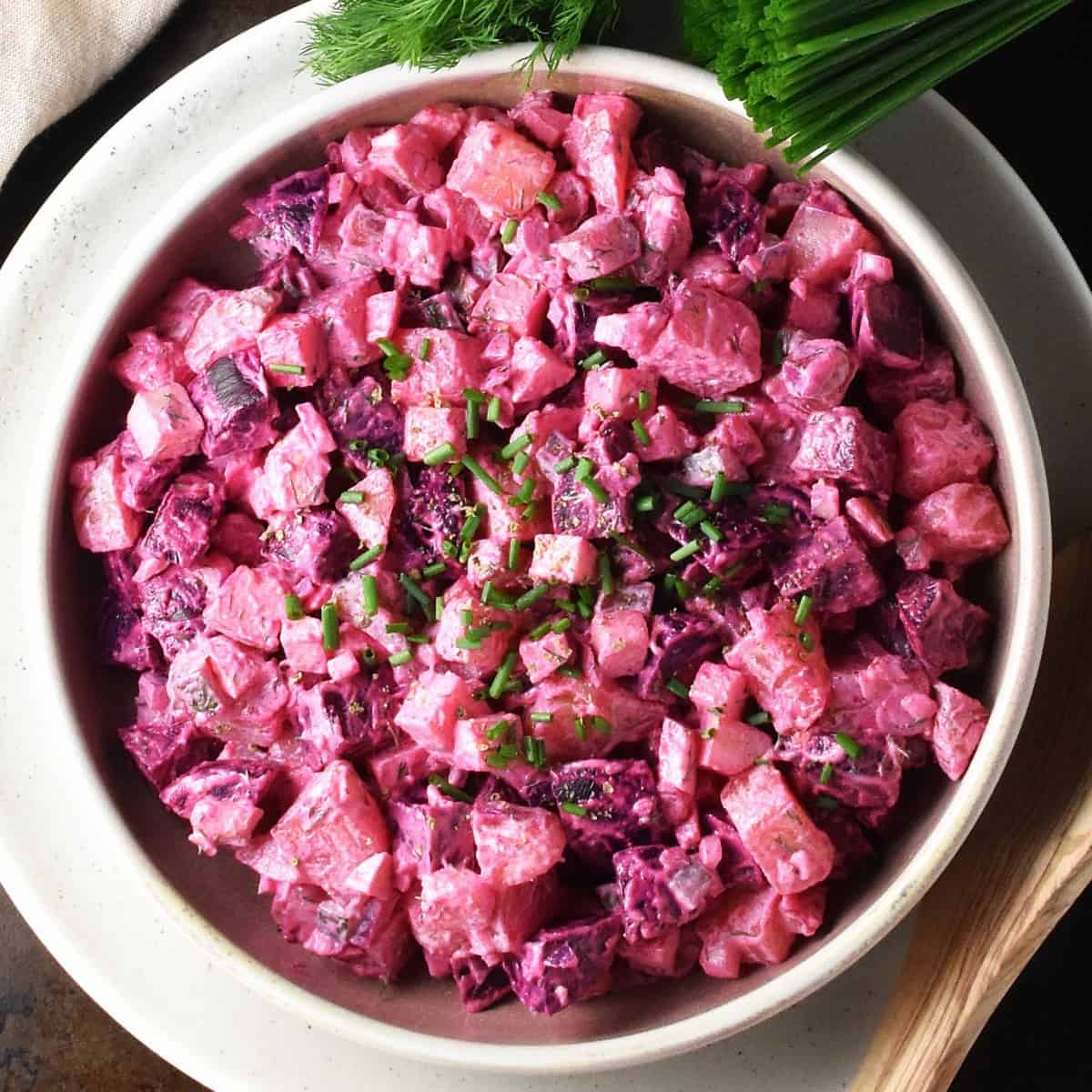 Top down view of creamy beet potato salad in shallow bowl with herbs in background.