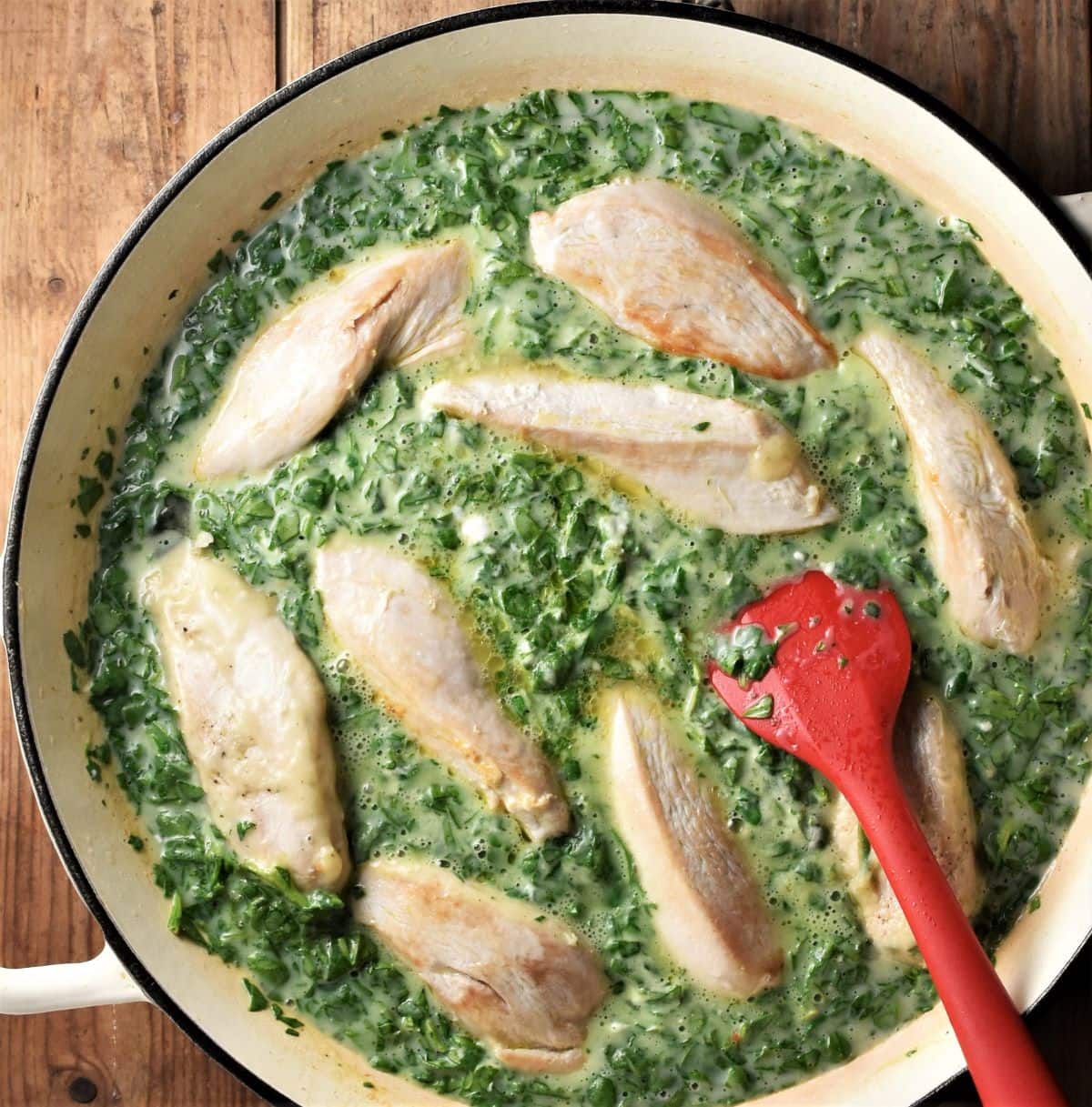 Chicken strips in creamy spinach sauce in large shallow pan with red spatula.