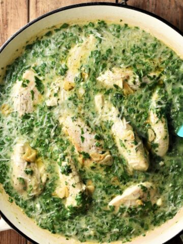 Creamy spinach chicken in large shallow pan with blue spoon.