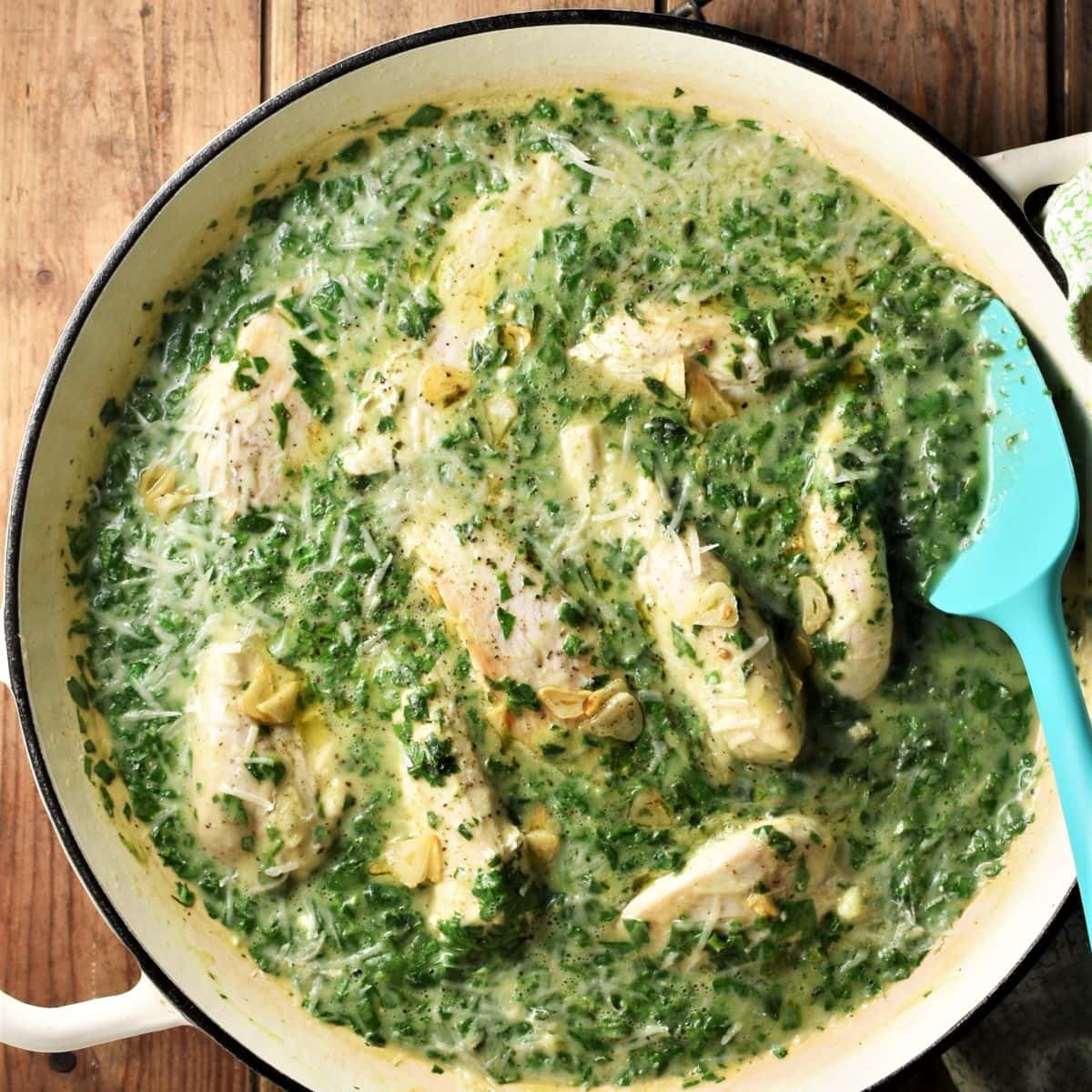 Creamy spinach chicken in large shallow pan with blue spoon.