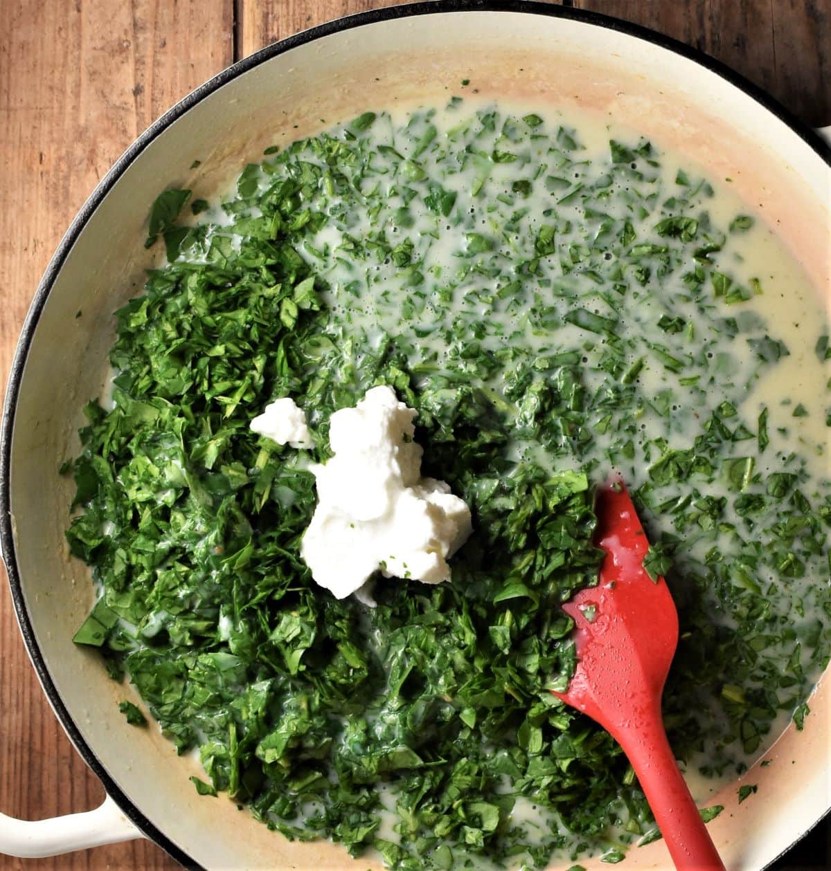 Making spinach sauce with yogurt in large shallow pan with red spatula.