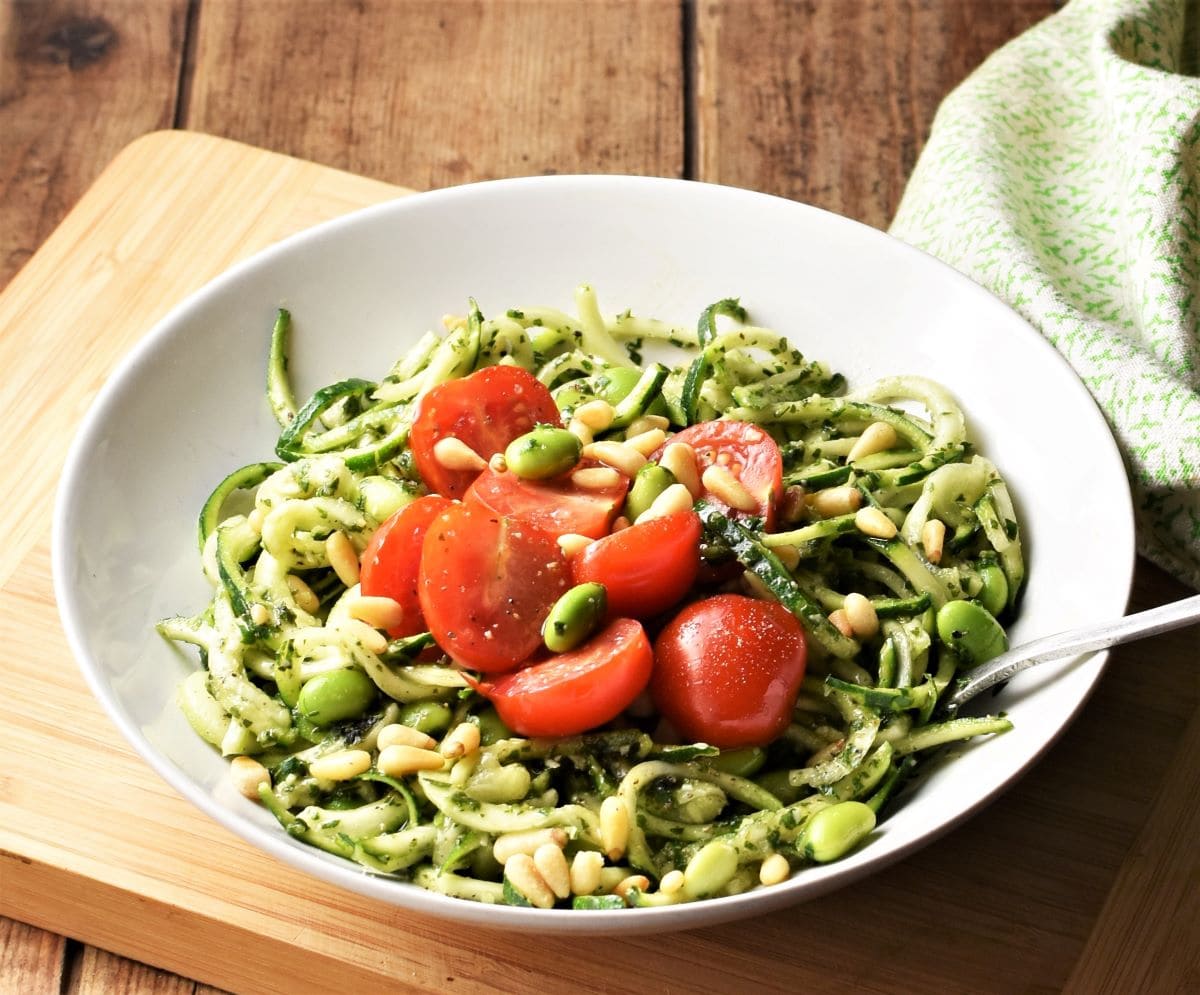 Zoodles with pesto, beans and cherry tomatoes in white bowl with fork.