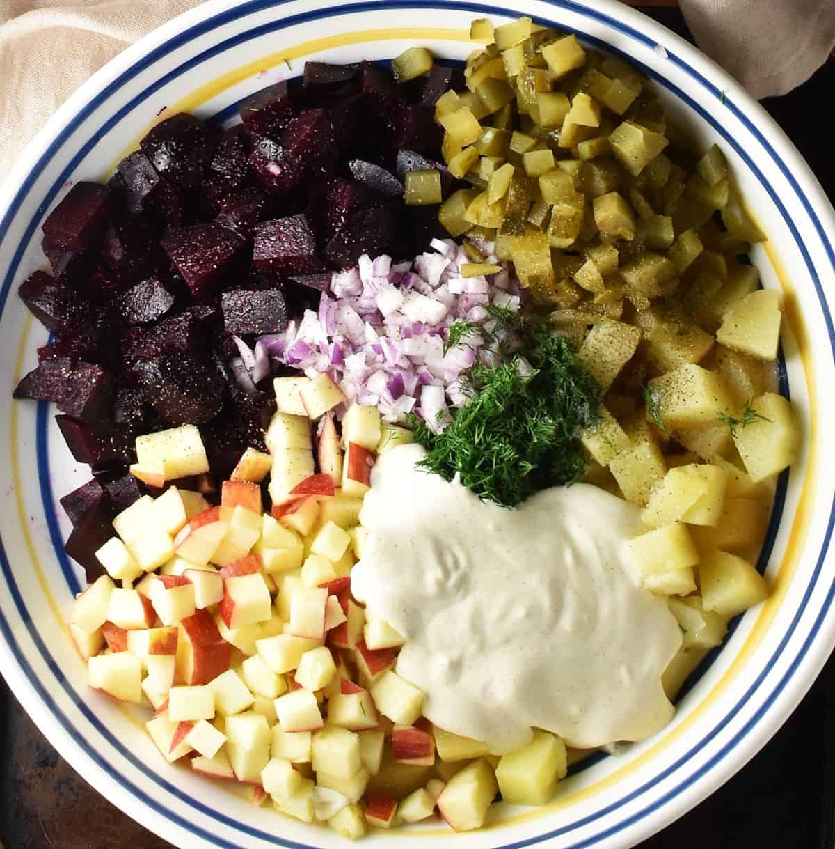 Cubed ingredients, fresh herbs and creamy dressing for beet and potato salad in shallow large bowl.