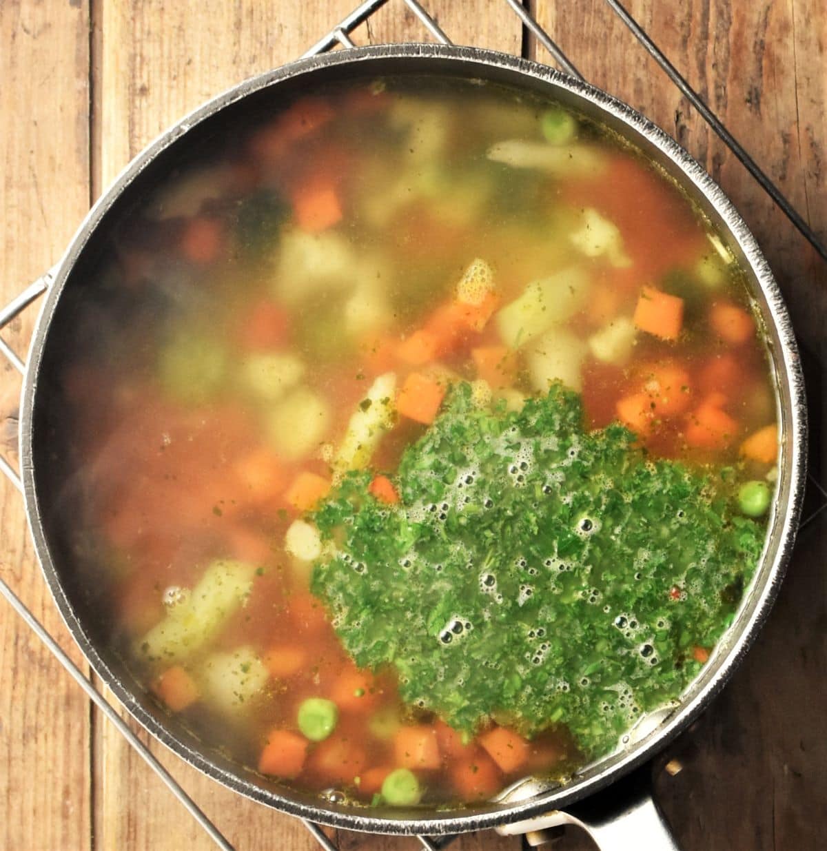 Making chunky vegetable soup in pot with fresh herbs.