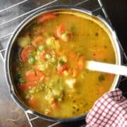 Top down view of frozen vegetable soup with chunks of veg in metal pot with ladle.