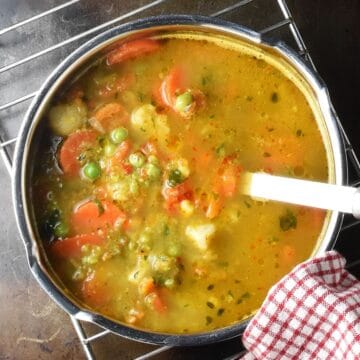 Top down view of frozen vegetable soup with chunks of veg in metal pot with ladle.