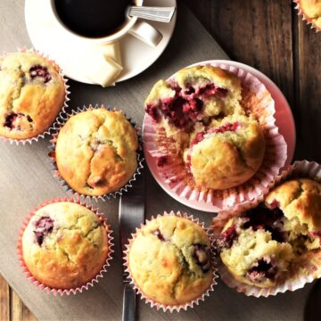 Top down view of raspberry white chocolate muffins in red liners and coffee in white cup.