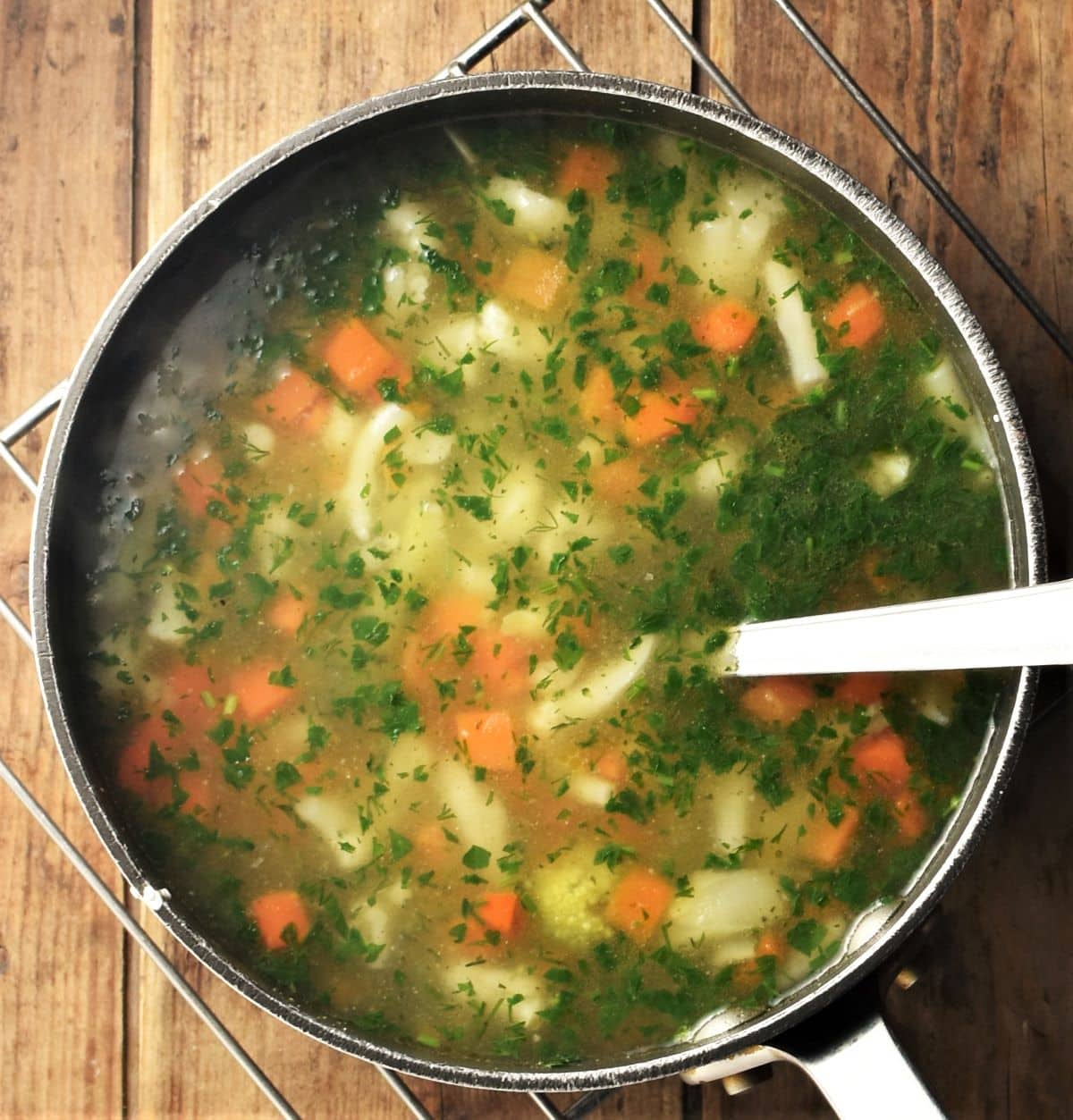 Simple chunky frozen vegetable soup with herbs in pot with spoon.