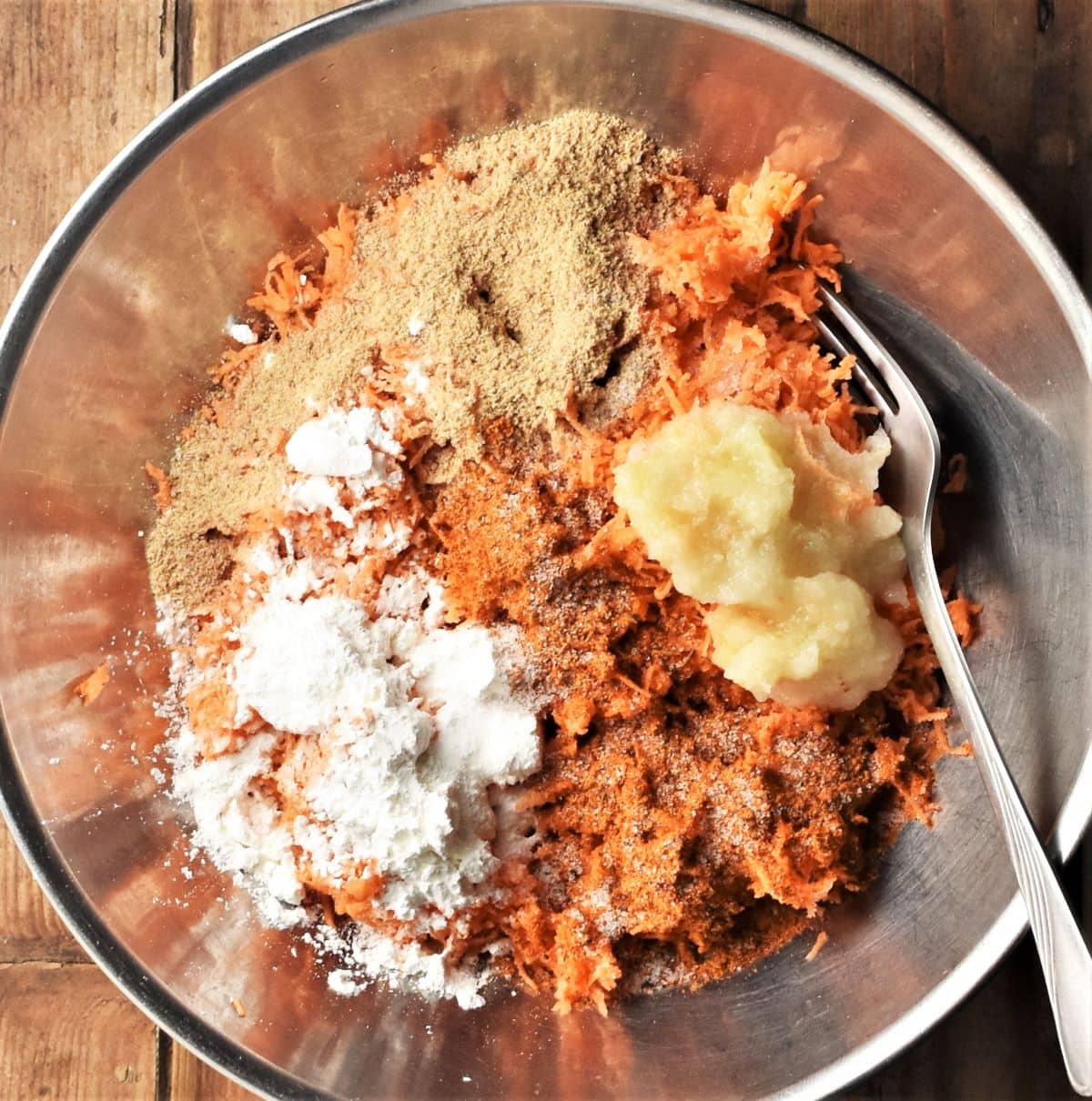 Finely grated sweet potato with spices for making fritters in metal bowl.