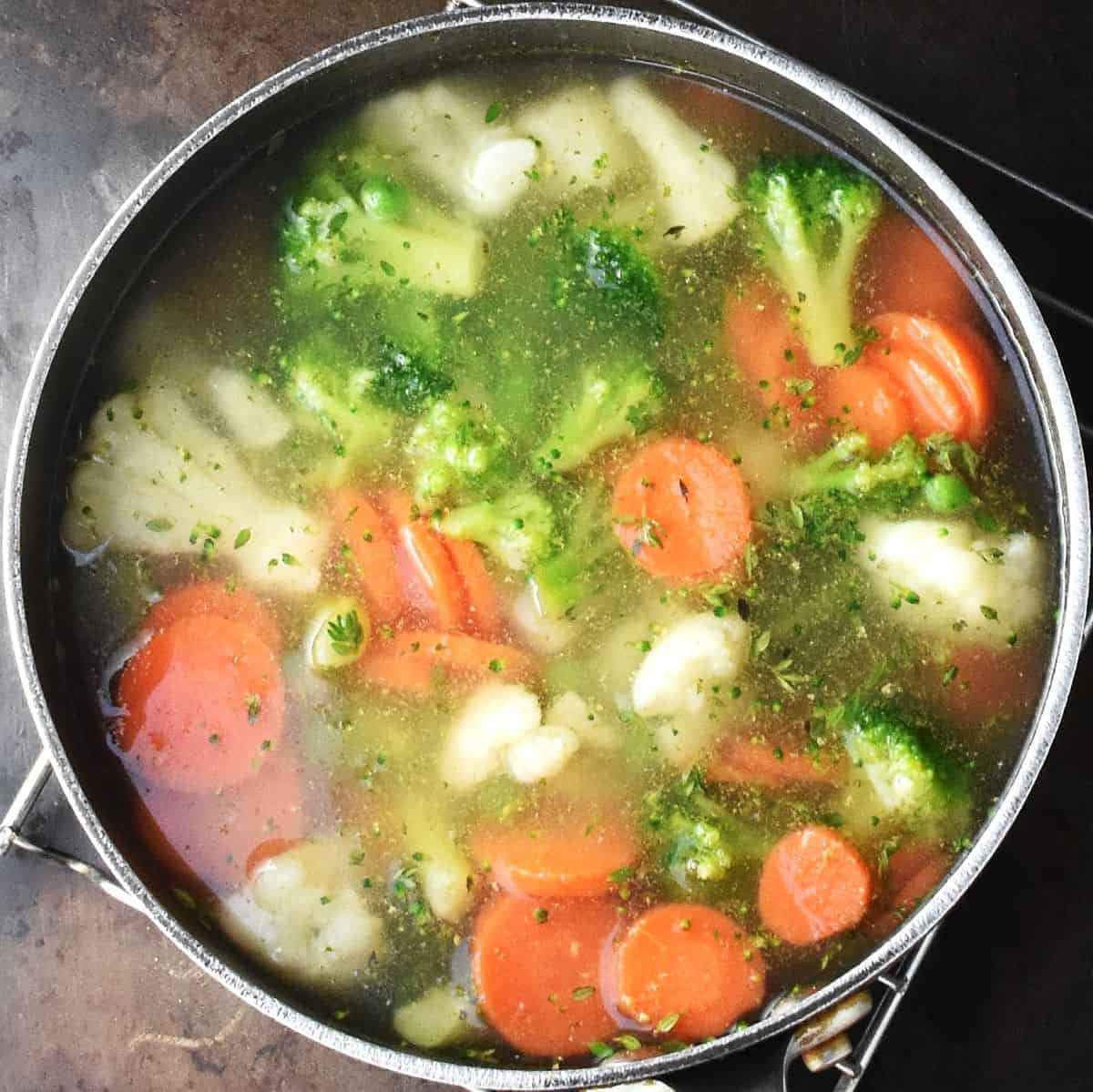 Chunks of vegetables with stock in large black pot.