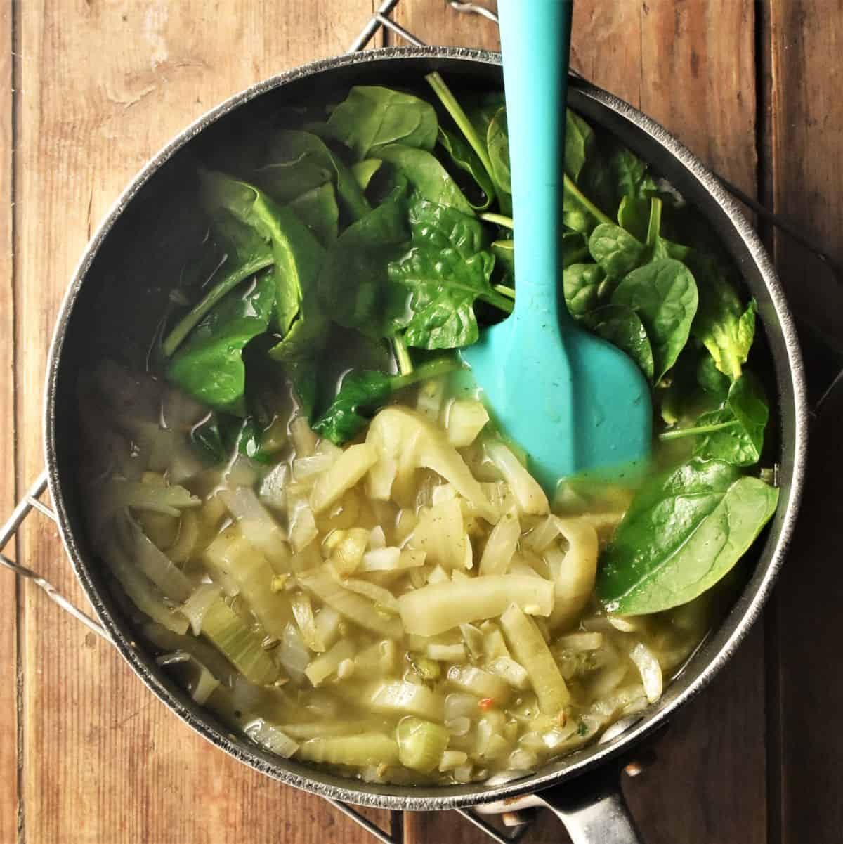 Adding spinach to chunky fennel soup in large pot with blue spoon.