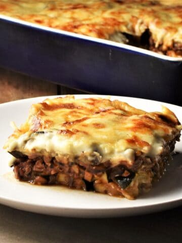 Side view of vegetarian moussaka slice on top of plate with moussaka in background.