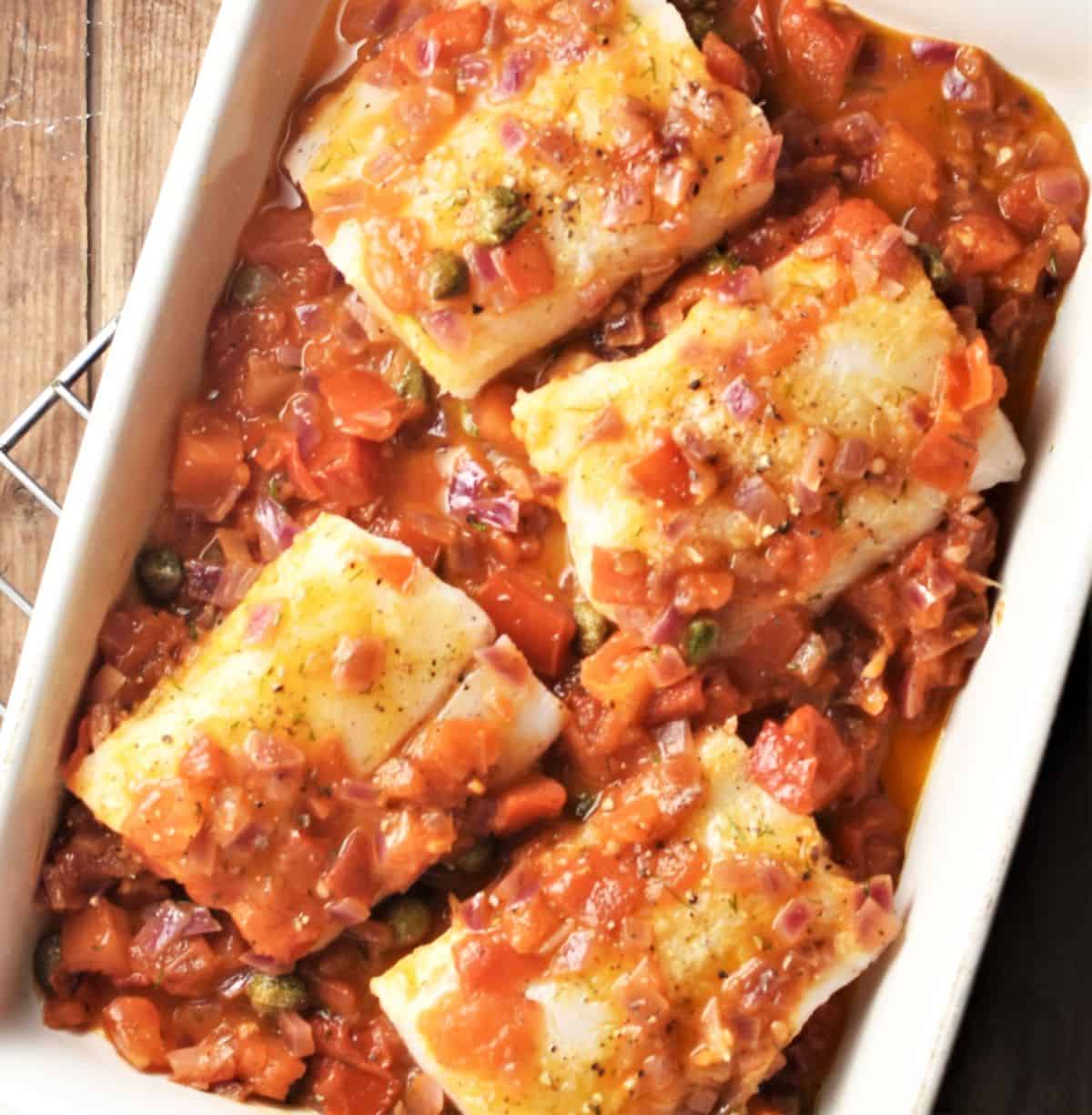 Top down view of 4 cod pieces in chunky tomato sauce in rectangular dish.