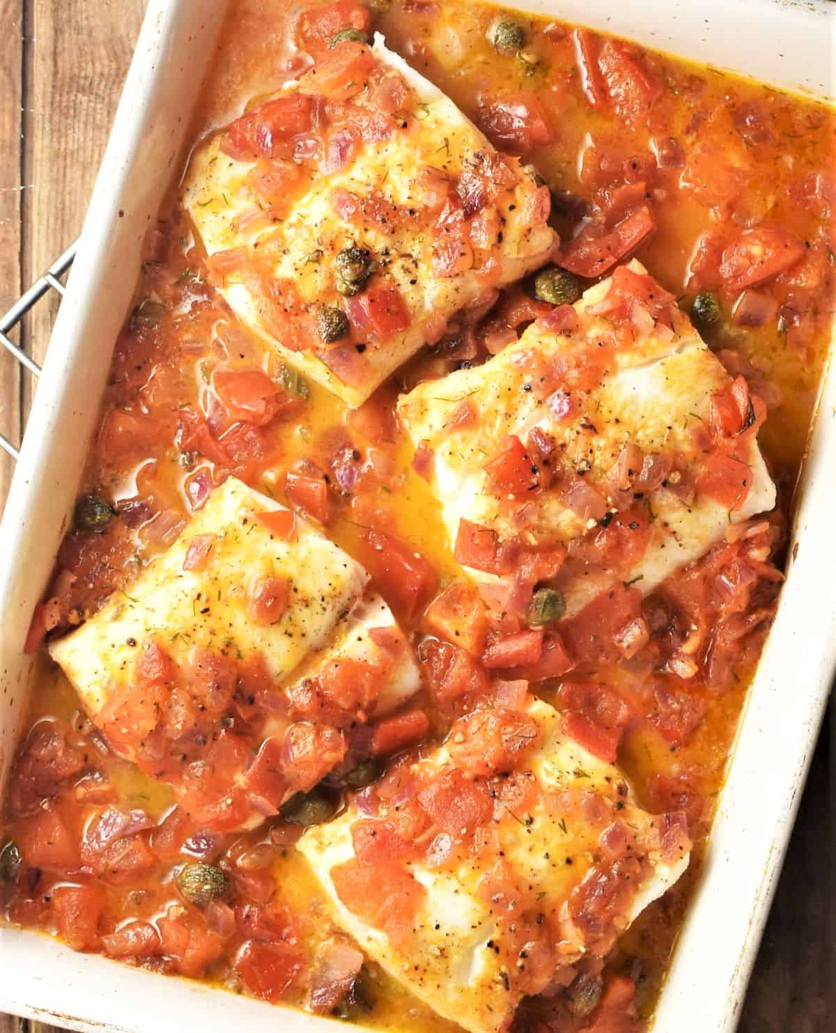 Baked cod in chunky tomato sauce in casserole dish.