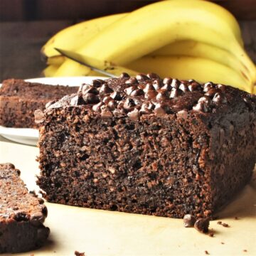 Side view of chocolate banana cake with bananas in background.