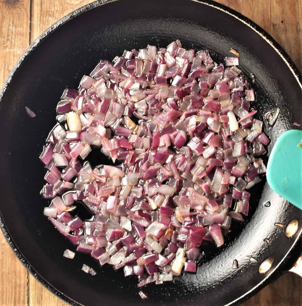 Sauteeing red onions in pan with blue spatula.