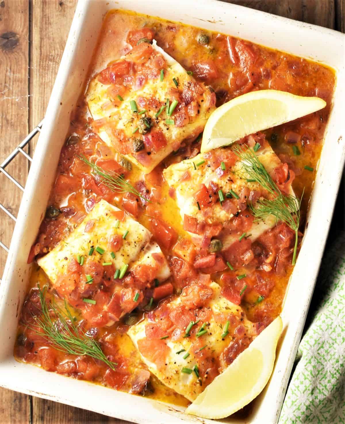 Fish pieces and lemon wedges with tomato sauce in casserole dish.
