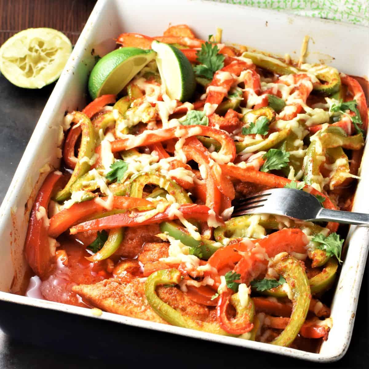 Side view of chicken fajitas casserole with fork and lime in background.