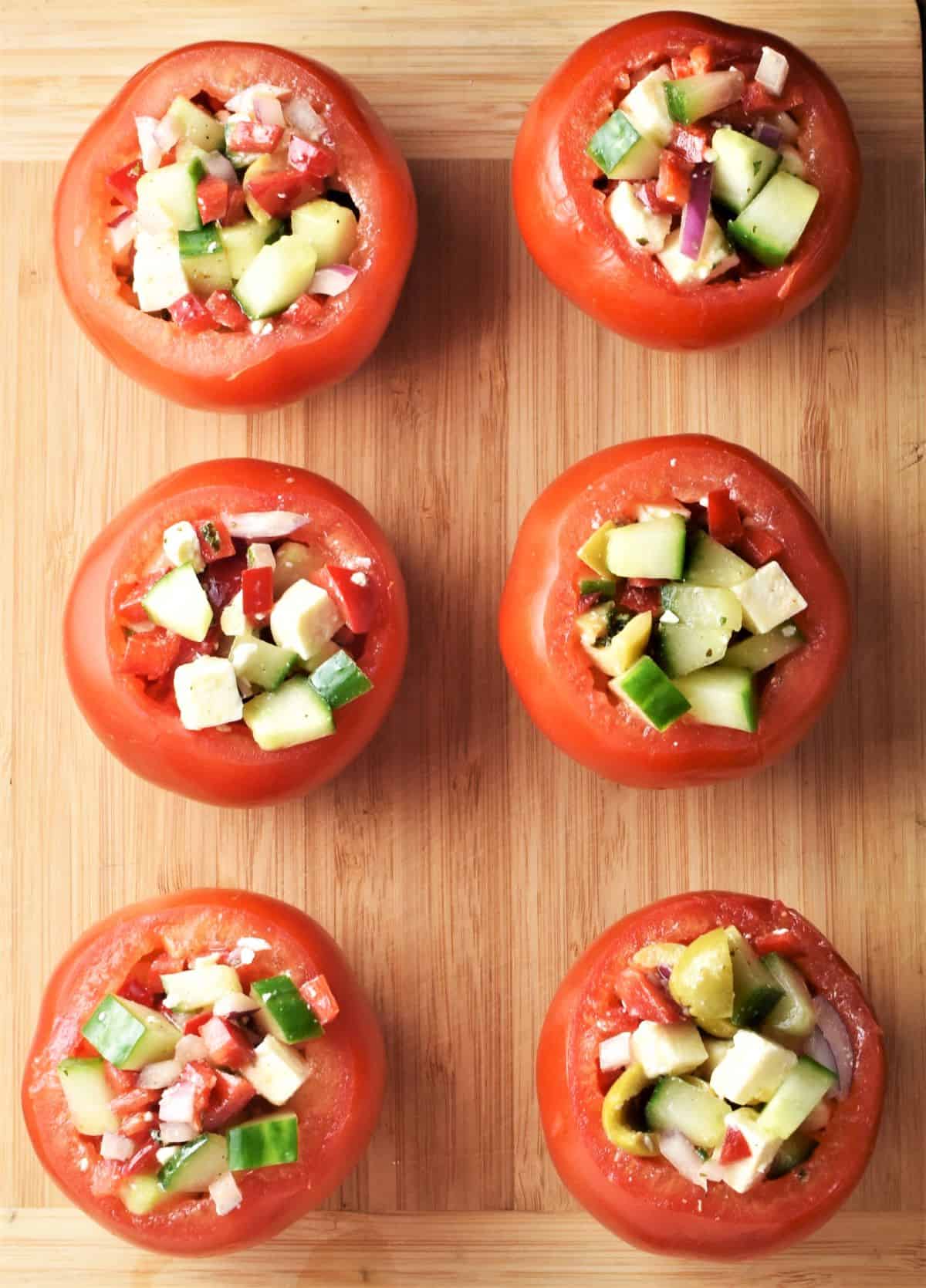 Top down view of 6 salad stuffed tomatoes on top of board.