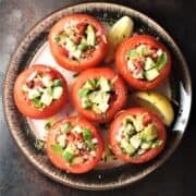 Top down view of vegetarian stuffed tomatoes with lemon wedges on brown plate.