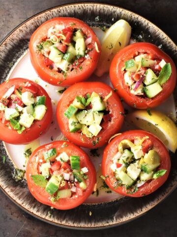 Top down view of vegetarian stuffed tomatoes with lemon wedges on brown plate.