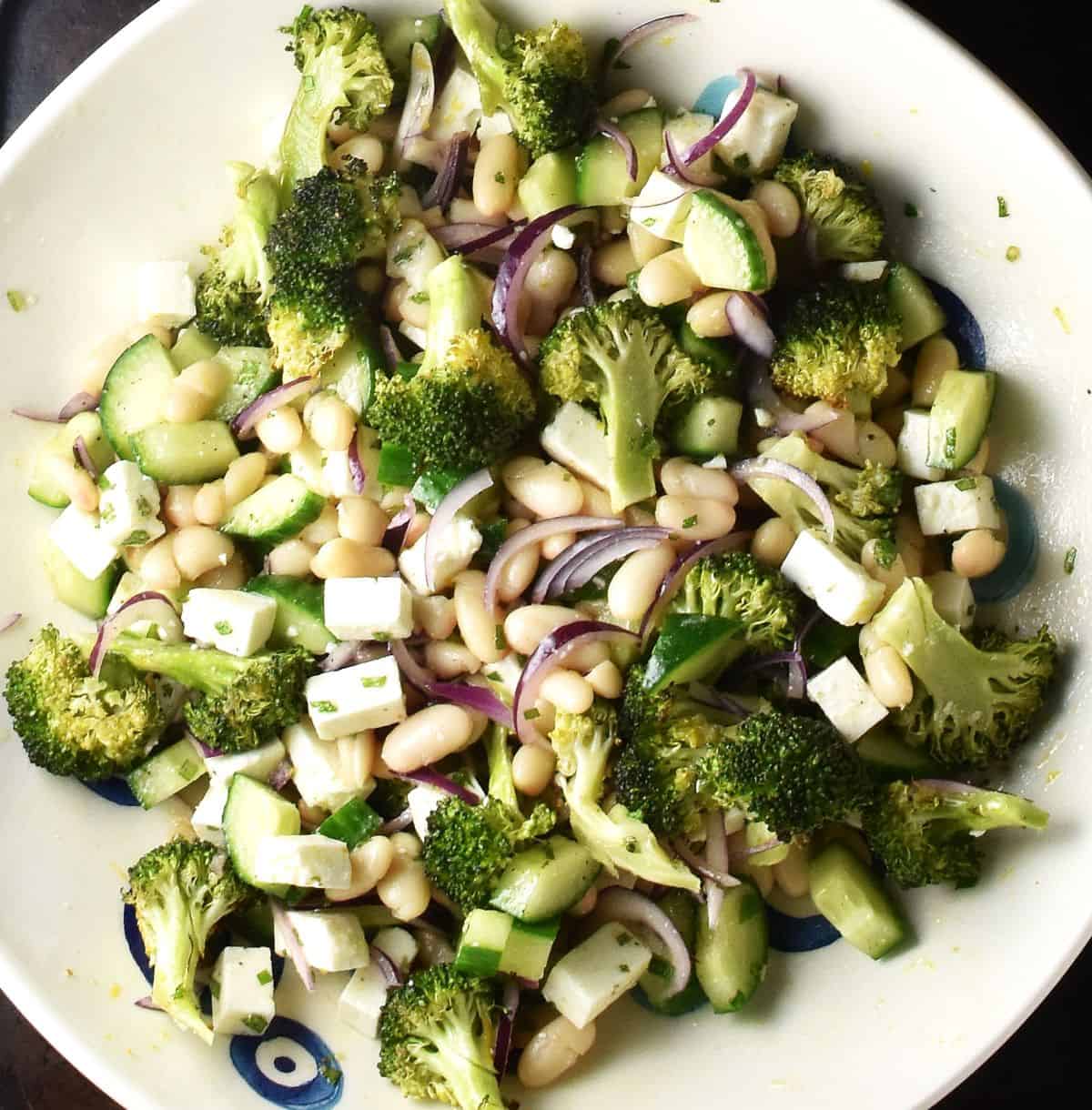 Assembled broccoli, bean and feta salad mixture in white shallow bowl.