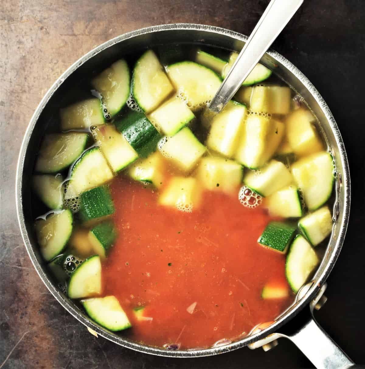 Cubed zucchini and tomato puree in pot with spoon.