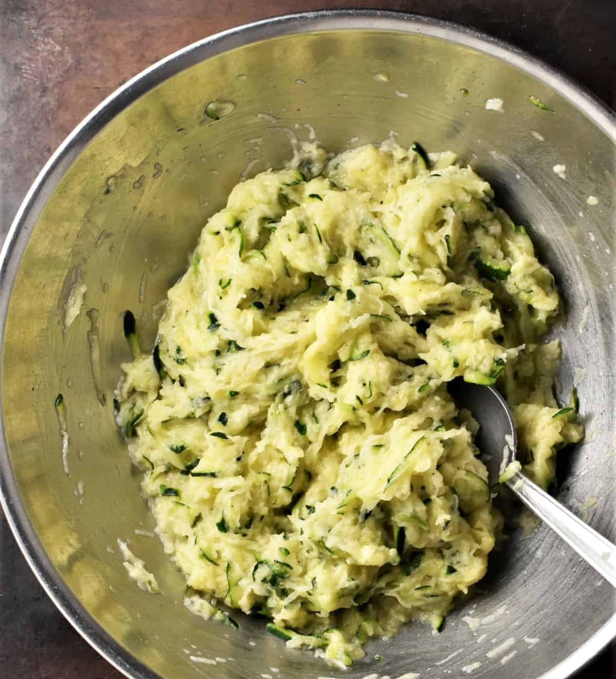 Potato zucchini fritters batter in metal bowl with spoon.