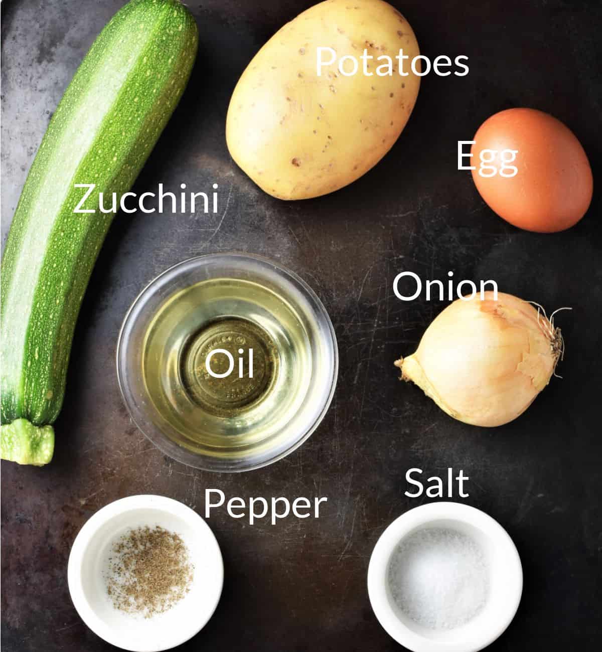 Ingredients for making potato zucchini fritters on top of dark metal surface.