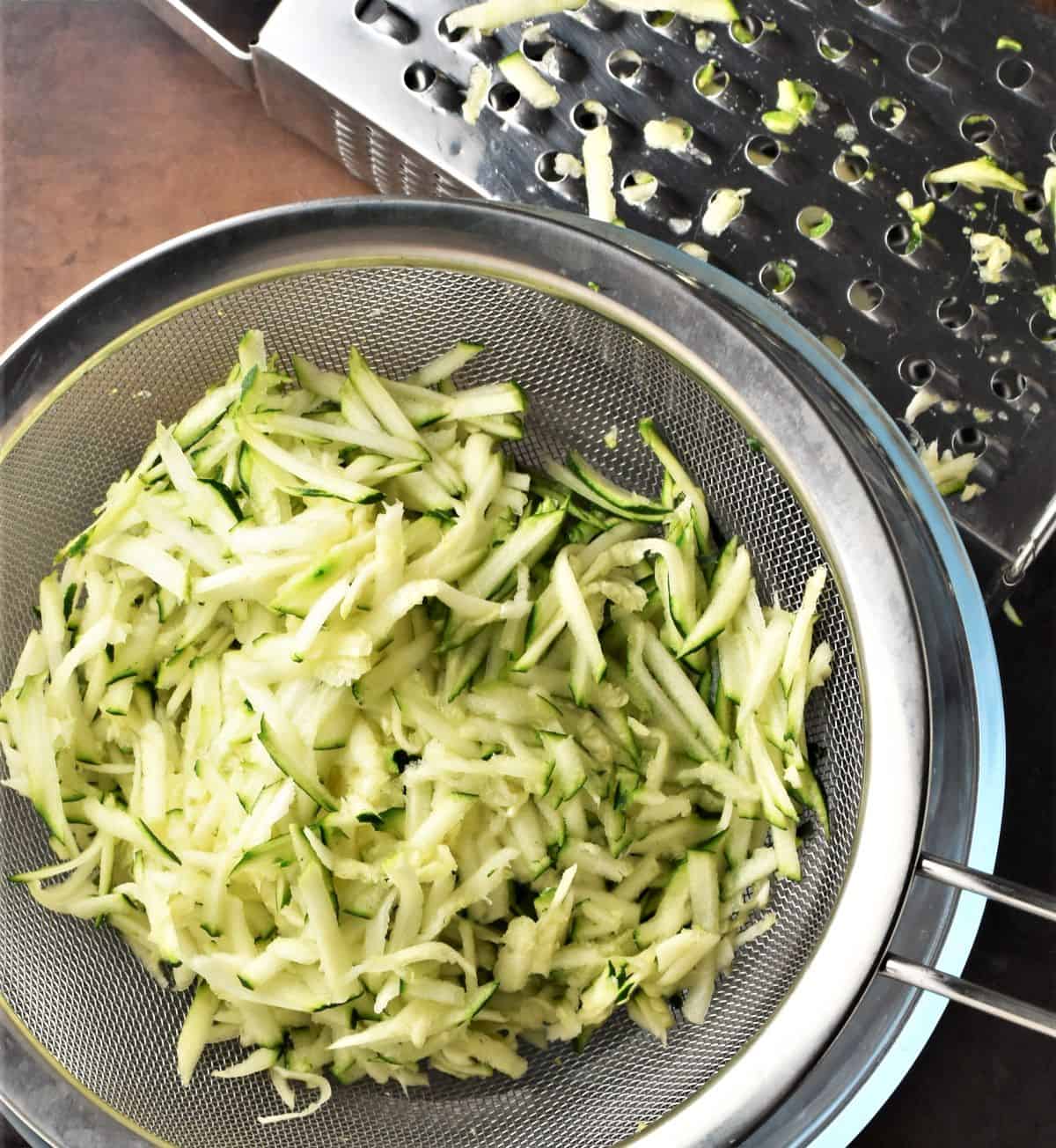 Shredded courgette in sieve with grater in background.