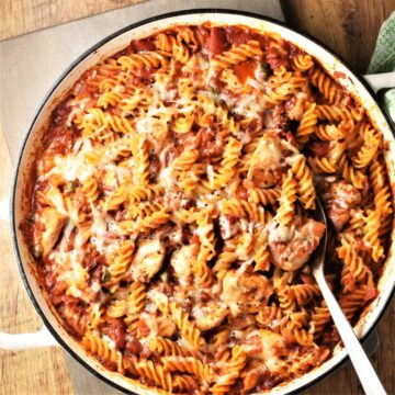 Top down view of chicken tomato pasta bake with spoon in large round dish.