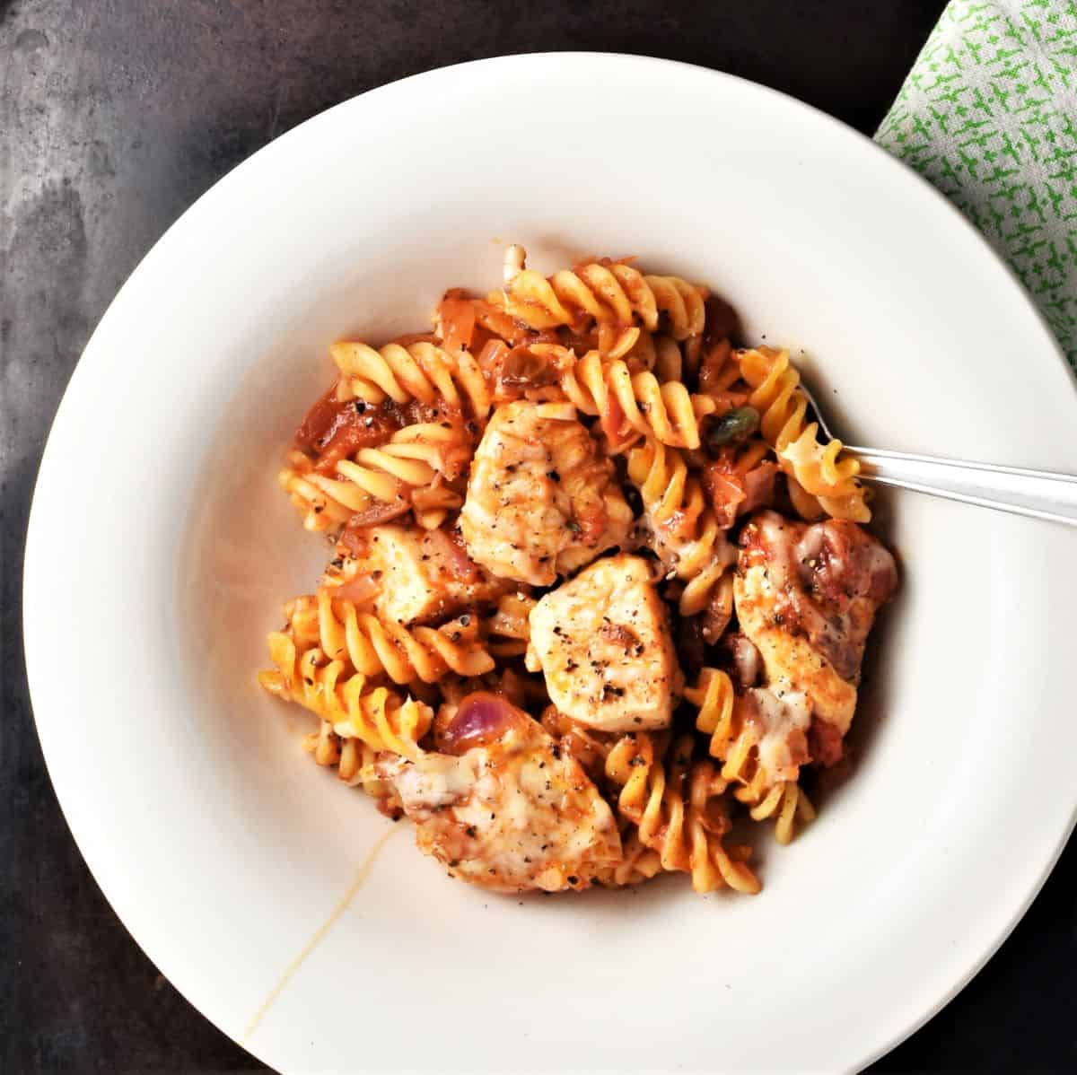 Chicken and pasta with tomato sauce in white dish.