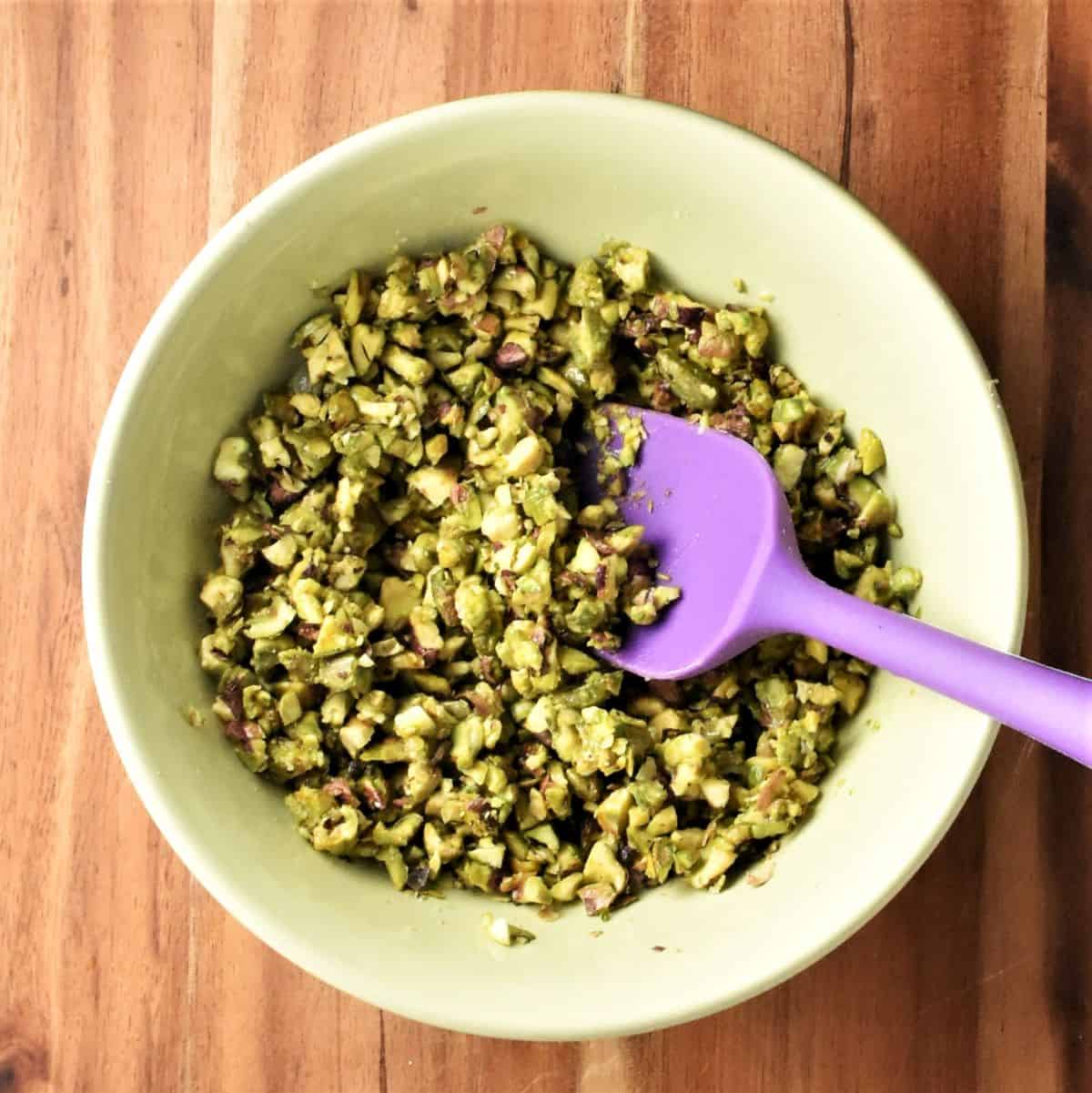 Chopped pistachios in green bowl with purple spoon.