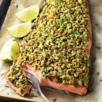 Top down view of pistachio crusted salmon side with lime wedges and fork.