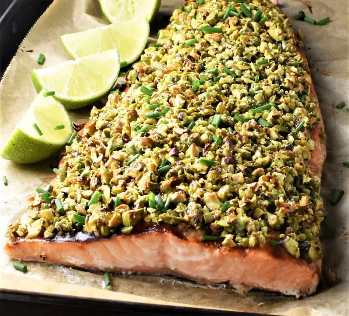 Side view of salmon with pistachios and lime on parchment.