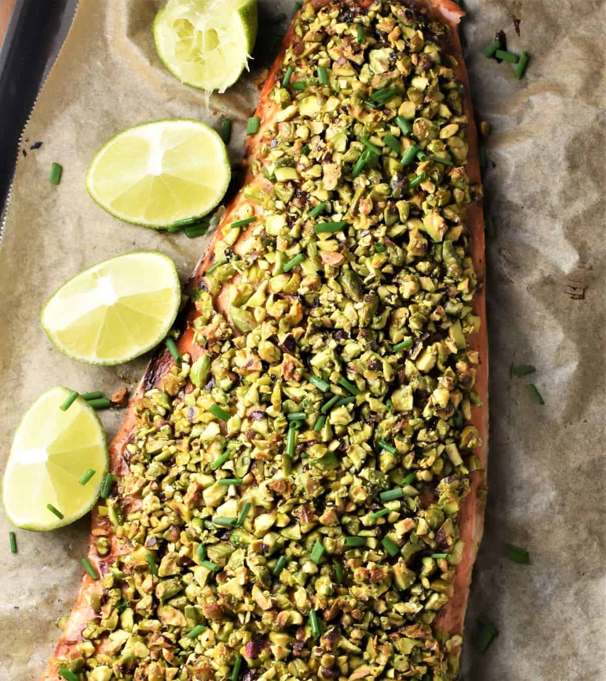 Top down view of pistachio salmon with lime wedges on top of parchment.
