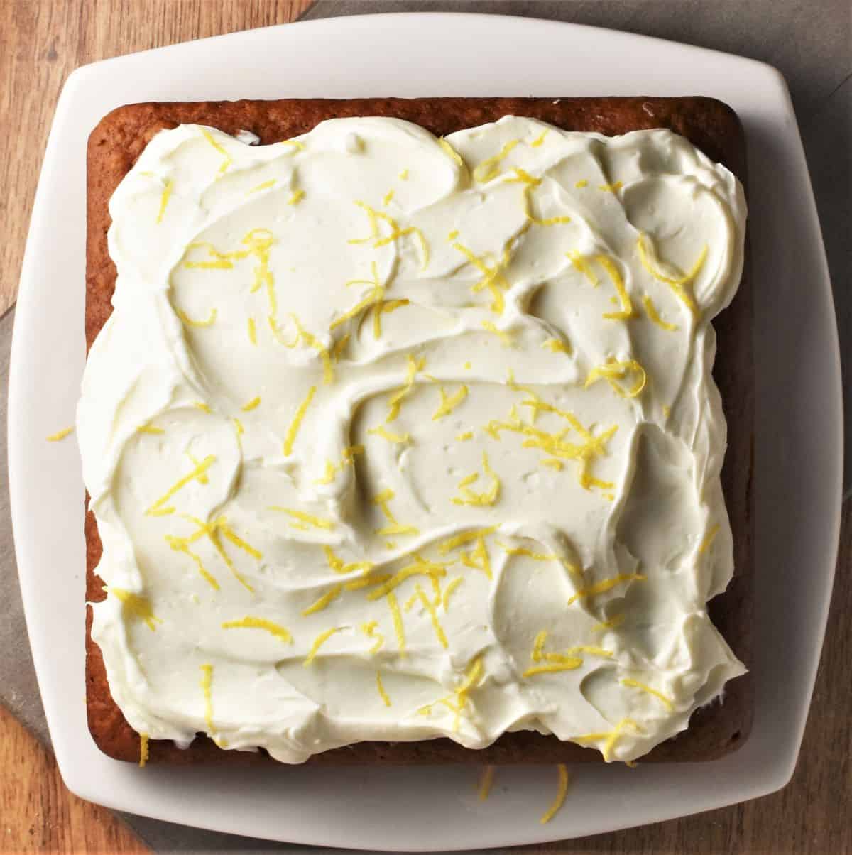 Top down view of pumpkin cake with cheese frosting on white plate.