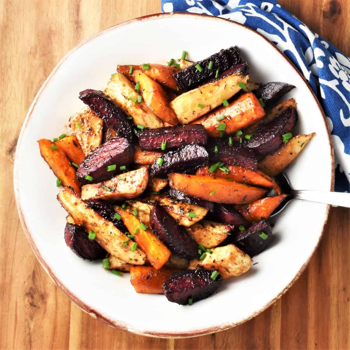 Top down view of sticky balsamic roasted vegetables in white bowl with spoon.
