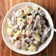 Top down view of herring salad in white bowl with spoon.