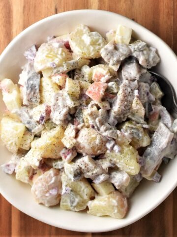 Top down view of herring salad in white bowl with spoon.